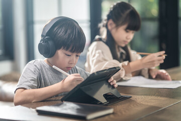 Asian little boy using tablet and headphones for E-learning at home.