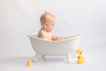 bathing the baby in white bath with foam and rubber ducks
