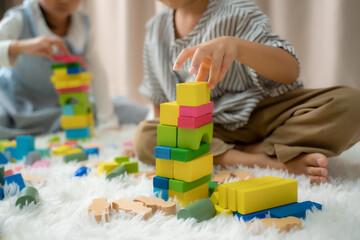 Children is happy to play toy building blocks while sitting on carpet at home.